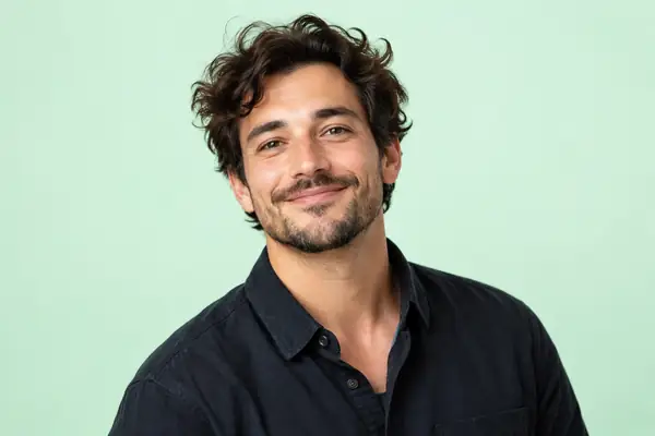 Friendly studio portrait of a creative professional in a dark shirt against a pale mint background.